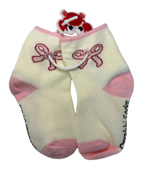 Pair of baby socks with pink bows and a small plush toy on a textured surface